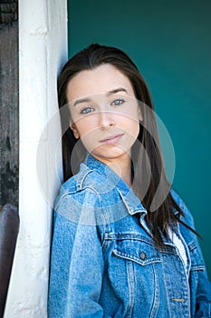 A beautiful teen brunette girl with a serious look leaning against a wall in thought with a teal green turquoise