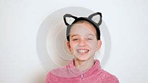A beautiful teen girl in cats ears headband is actively telling something and looking at the camera. The girl sings or