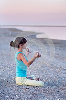 Beautiful teen girl doing yoga exercise lotus pose on the background of the sea at sunset,