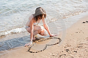 Beautiful teen girl draw love shape on sand
