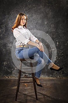 Beautiful teen girl dressed in blue jeans and white shirt sitting on chair studio portrait.