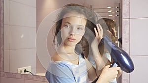 Beautiful teen girl dries hair a hairdryer in bathroom