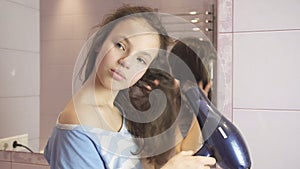 Beautiful teen girl dries hair a hairdryer in bathroom