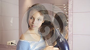 Beautiful teen girl dries hair a hairdryer in bathroom