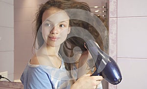 Beautiful teen girl dries hair a hairdryer in bathroom