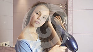 Beautiful teen girl dries hair a hairdryer in bathroom