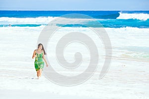 Beautiful teen girl in green dress walking along Hawaiian beach