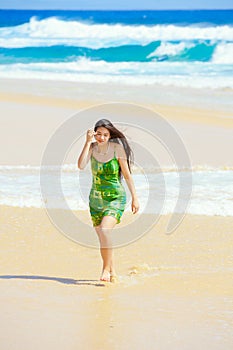 Beautiful teen girl in green dress walking along Hawaiian beach