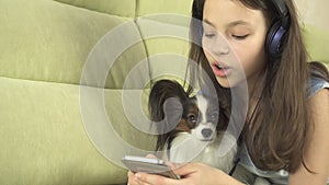 Beautiful teen girl in headphones singing karaoke songs in smartphone with dog