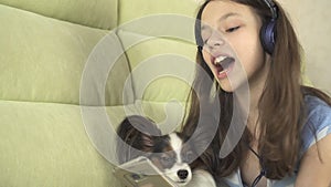 Beautiful teen girl in headphones singing karaoke songs in smartphone with dog
