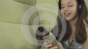 Beautiful teen girl in headphones singing karaoke songs in smartphone with dog stock footage video