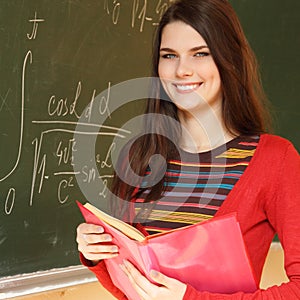 beautiful teen girl high achiever in classroom near desk with formulas of higher mathematics