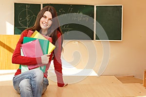 Beautiful teen girl high achiever in classroom near desk happy s