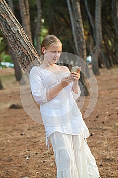 Beautiful teen girl listening to music. Young girl outside in park listening to music on headphones on nature background