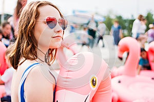 Beautiful teen girl in pink heart shaped glasses on inflatable Flamingo enjoys summer vacation