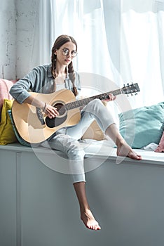 beautiful teen girl playing acoustic guitar while sitting on windowsill photo