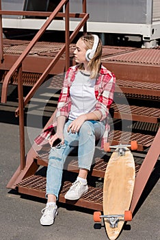 beautiful teen girl in red plaid shirt and headphones sitting on stairs