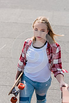 beautiful teen girl in red plaid shirt walking with skateboard