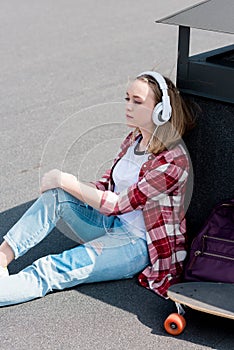 beautiful teen girl with skateboard sitting on rooftop and listening music