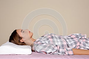 Beautiful teen girl sleeping with orthopedic pillow on bed against color background