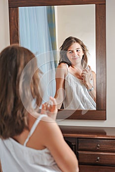 A beautiful teen girl studies her appearance as she looks into the mirror