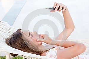 Beautiful teen girl takes a selfie on the phone lying in a hammock