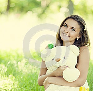 Beautiful teen girl with Teddy bear in the park at green grass.