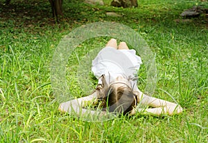 Beautiful teen girl in white dress lying on green grass. Boho style portrait