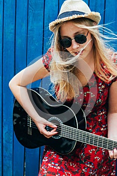 Beautiful teenage blonde long haired girl playing acoustic guitar outdoor. Vertical image