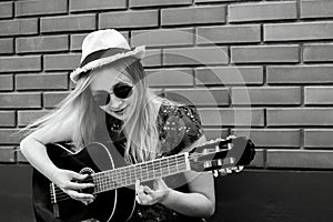 Beautiful teenage blonde long haired girl playing acoustic guitar outdoor. Vertical black and white color image.