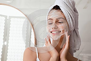 Beautiful teenage girl applying cleansing foam onto face in bathroom, space for text. Skin care cosmetic