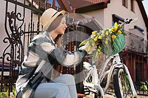Beautiful teenage girl with bouquet of yellow tulips and bicycle outdoors near house