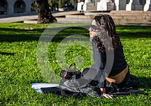 Beautiful teenage girl with dark hair and sun glasses sitting in a public garden