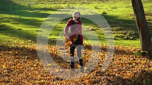 Beautiful teenage girl having fun playing in the autumn forest. She throws fallen yellow leaves into the air. The girl