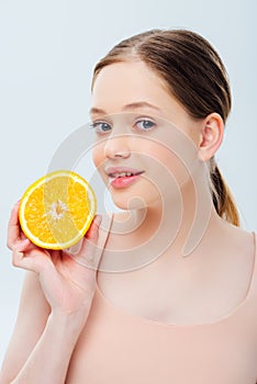 Beautiful teenage girl holding ripe orange half isolated on grey