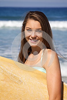 Beautiful Teenage Girl Holding a Surfboard at the Beach Smiling