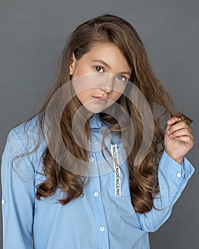 A beautiful teenage girl holds a lock of long thick hair with curls in her hand, looking into the frame. Brown-haired person.