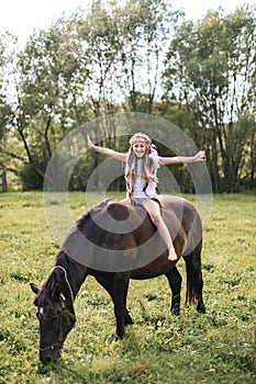 Beautiful teenage girl with long hair abd boho accessories riding horse at the field in summer. Horse riding, childhood