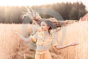 Beautiful teenage girl with long hair walking through a wheat field on a sunny day. Outdoors portrait. Schoolgirl relaxing