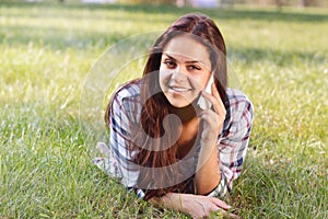 Beautiful teenage girl lying on field of green grass and talk by phone