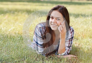 Beautiful teenage girl lying on field of green grass and talk by phone