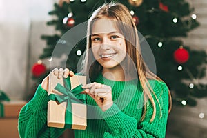 Beautiful teenage girl opens a gift made of kraft paper tied with a green ribbon, new year mood. Holiday concept of Christmas and