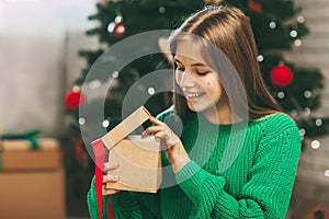 Beautiful teenage girl opens a gift made of kraft paper tied with a red ribbon, new year mood. Holiday concept of Christmas and