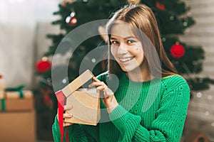 Beautiful teenage girl opens a gift made of kraft paper tied with a red ribbon, new year mood. Holiday concept of Christmas and