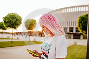 A beautiful teenage girl with pink hair looks at the phone and laughs