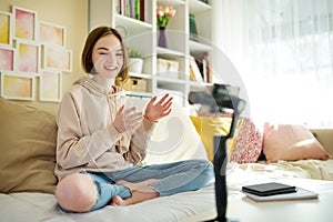 Beautiful teenage girl recording video blog with her smartphone. Young vlogger shooting vlog at home. Teen influencer creating