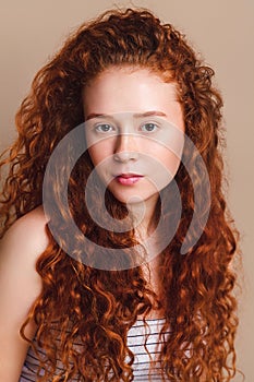 Beautiful teenage girl with red curly hair and brown eyes without makeup. Portrait shot in studio on a beige background.