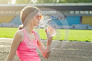 Beautiful teenage girl resting after workout at stadium, girl sat down to relax, drinking water