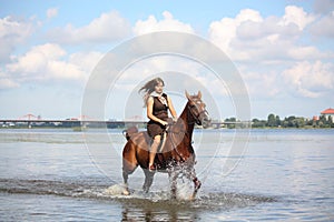 Beautiful teenage girl riding horse in the river