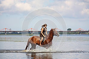 Beautiful teenage girl riding horse in the river